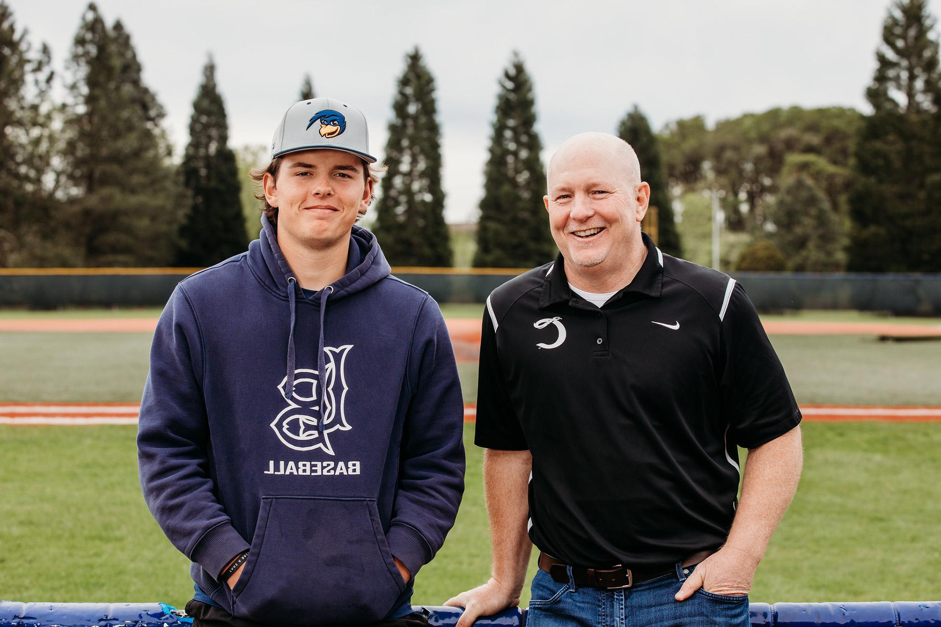 丹·西格尔和他的儿子卡登·西格尔站在棒球场上对着镜头微笑的照片